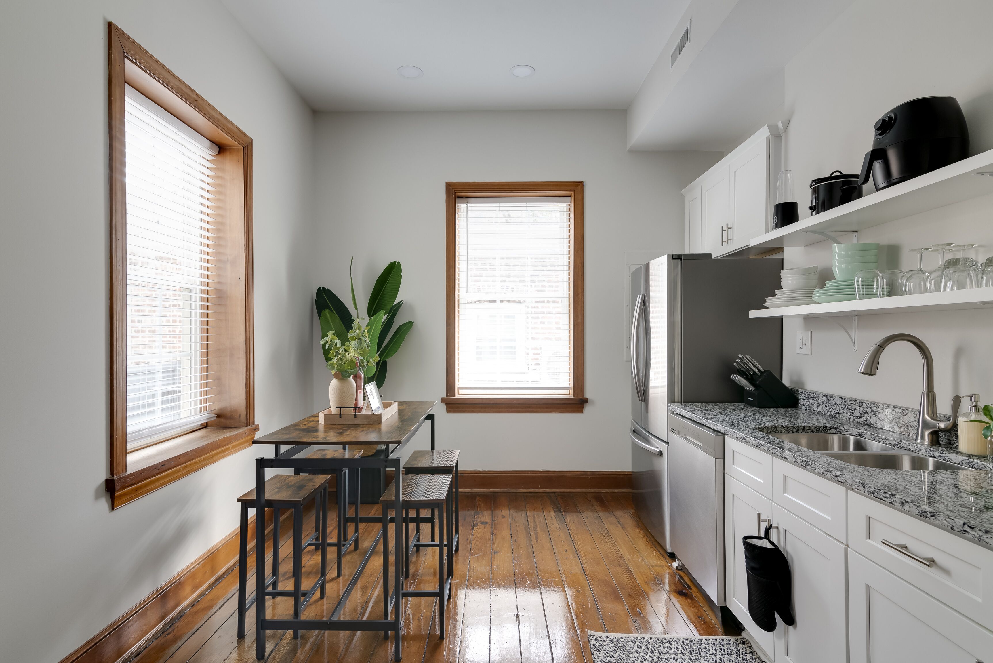 A compact kitchen with wooden flooring, white cabinets, a granite countertop, and a built-in dishwasher.