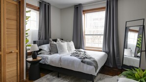 Ein Schlafzimmer mit Bett, Nachttisch, Lampe und Vorhängen.