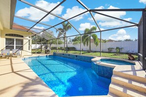 A swimming pool with a glass enclosure, a covered patio area, and a view of the backyard.