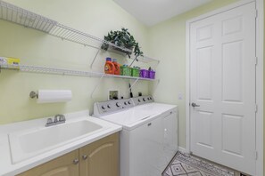 A laundry area with a washing machine, a sink, and shelves with laundry supplies.