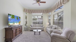A living room with a TV, two couches, a coffee table, and a ceiling fan. - Traditional Inland Home | Pool/Spa/Steps to Shops (Marco Island)
