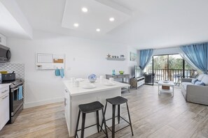 A modern kitchen with a central island, bar stools, and a dining area with a sofa and table.