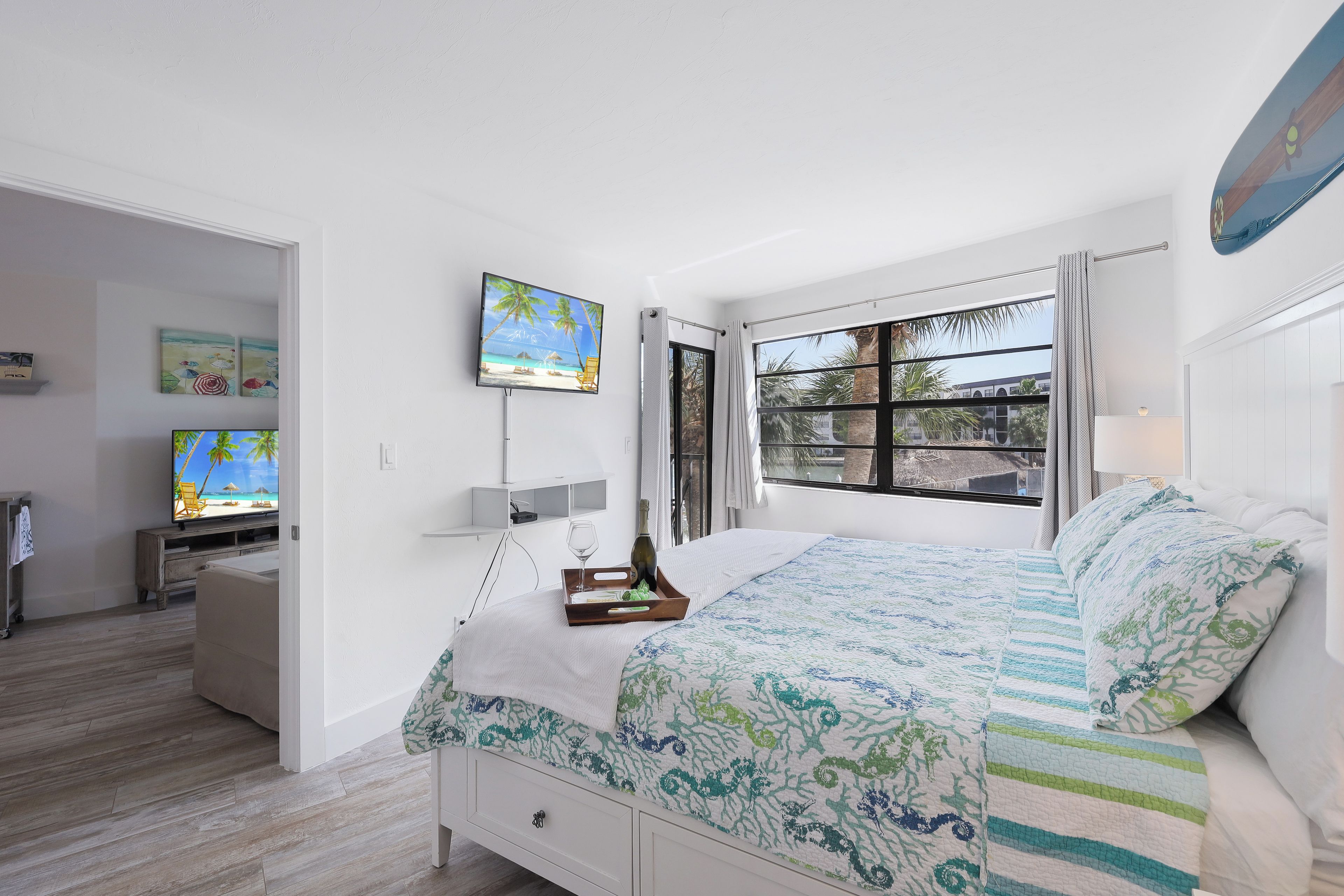 A bedroom with a bed, a TV, a window with curtains, and artwork on the wall.