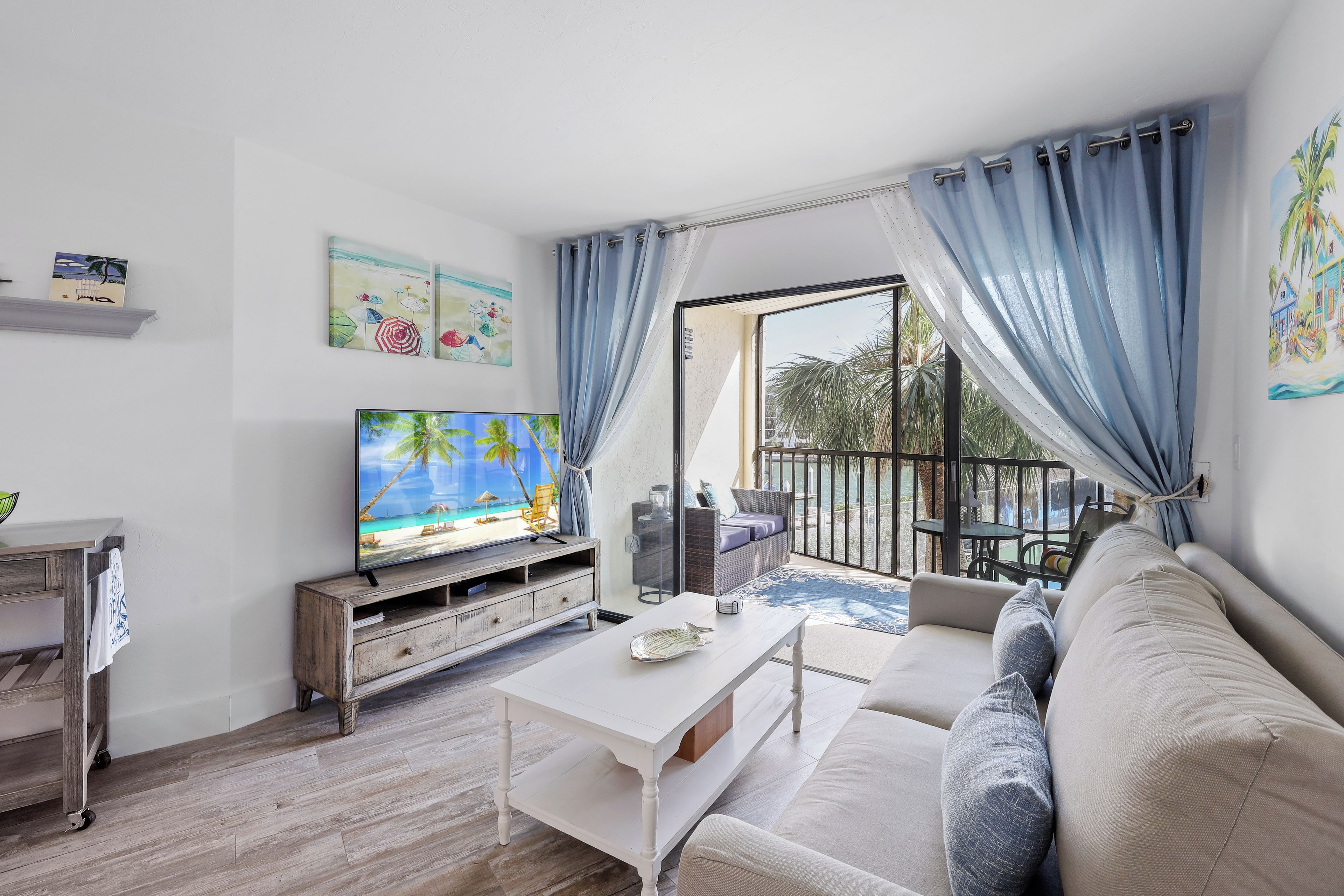 A living room with a television, a sofa, a coffee table, and a view of the outdoors.