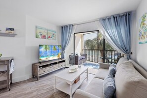 A living room with a television, a sofa, a coffee table, and a view of the outdoors.