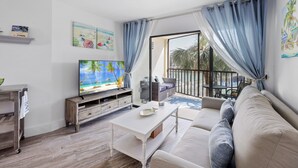 A living room with a television, a sofa, a coffee table, and a view of the outdoors. - Island-Style Riverfront Condo | Pools & Spas (Marco Island)