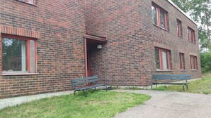 A brick building with a red door and windows, a bench, and a paved path. - THE Roomz  (Kotka)