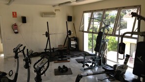 Ein Fitnessraum mit Trainingsgeräten, einem Feuerlöscher und einem Fenster mit Blick auf Gebäude und Bäume.