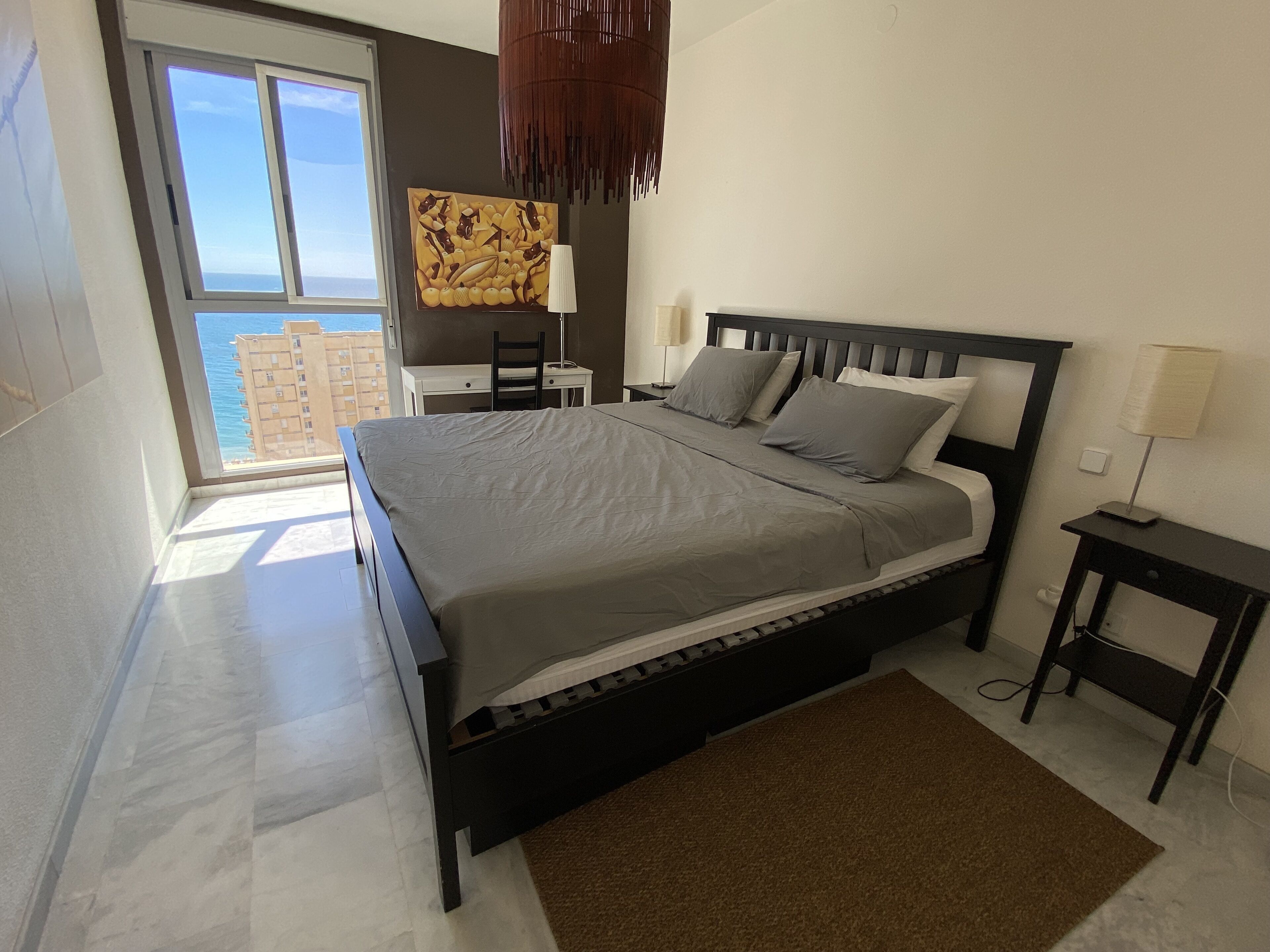 Ein Schlafzimmer mit Bett, Schreibtisch, Stuhl, Lampe und Meerblick.