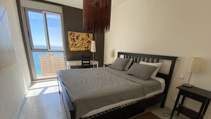 Ein Schlafzimmer mit Bett, Schreibtisch, Stuhl, Lampe und Meerblick.