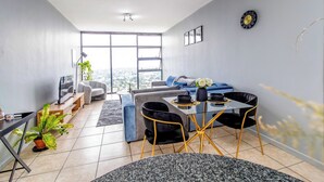 Een moderne woonkamer met een bank, een eettafel en stoelen. Een groot raam biedt uitzicht op de stad.