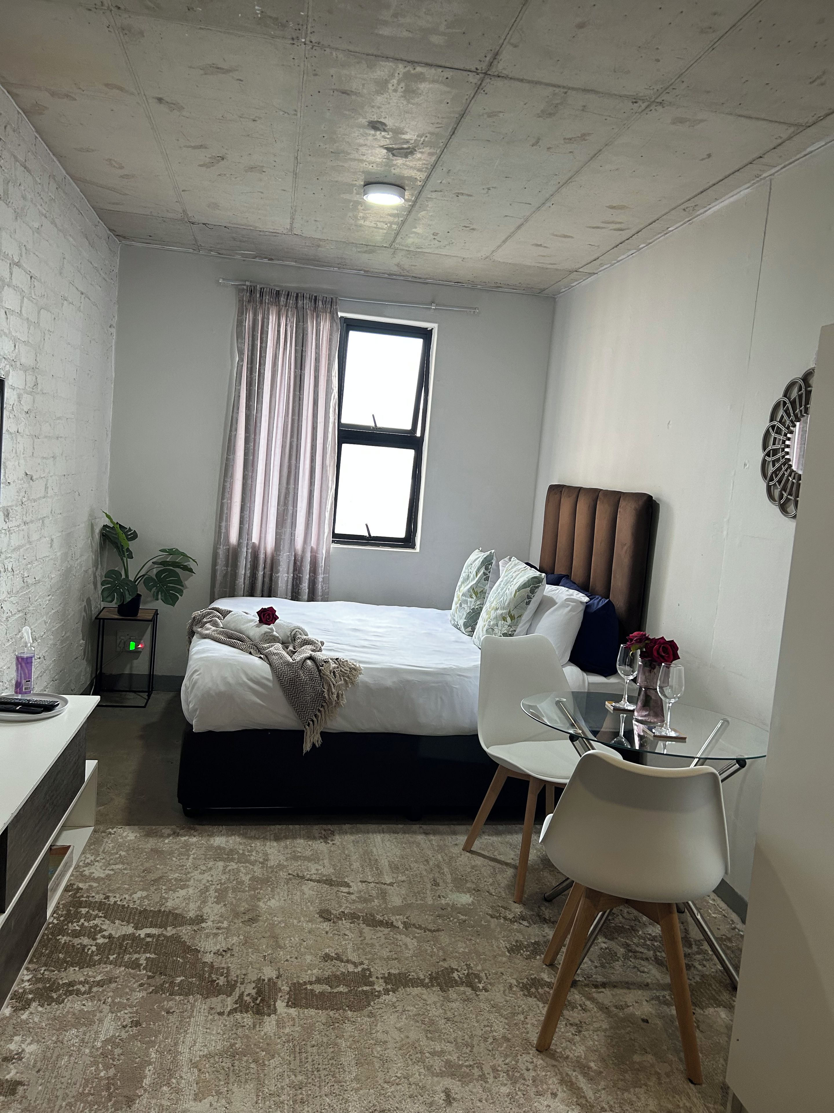Un dormitorio con cama, mesita de noche, silla y una pequeña mesa con un florero.