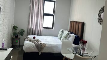 Un dormitorio con cama, mesita de noche, silla y una pequeña mesa con un florero.