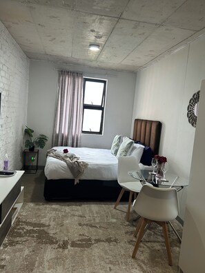 A bedroom with a bed, bedside table, chair, and a small table with a vase. - Views from The 509 (Johannesburg)