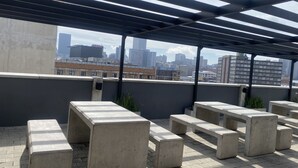 A rooftop terrace with concrete benches and a city skyline view.