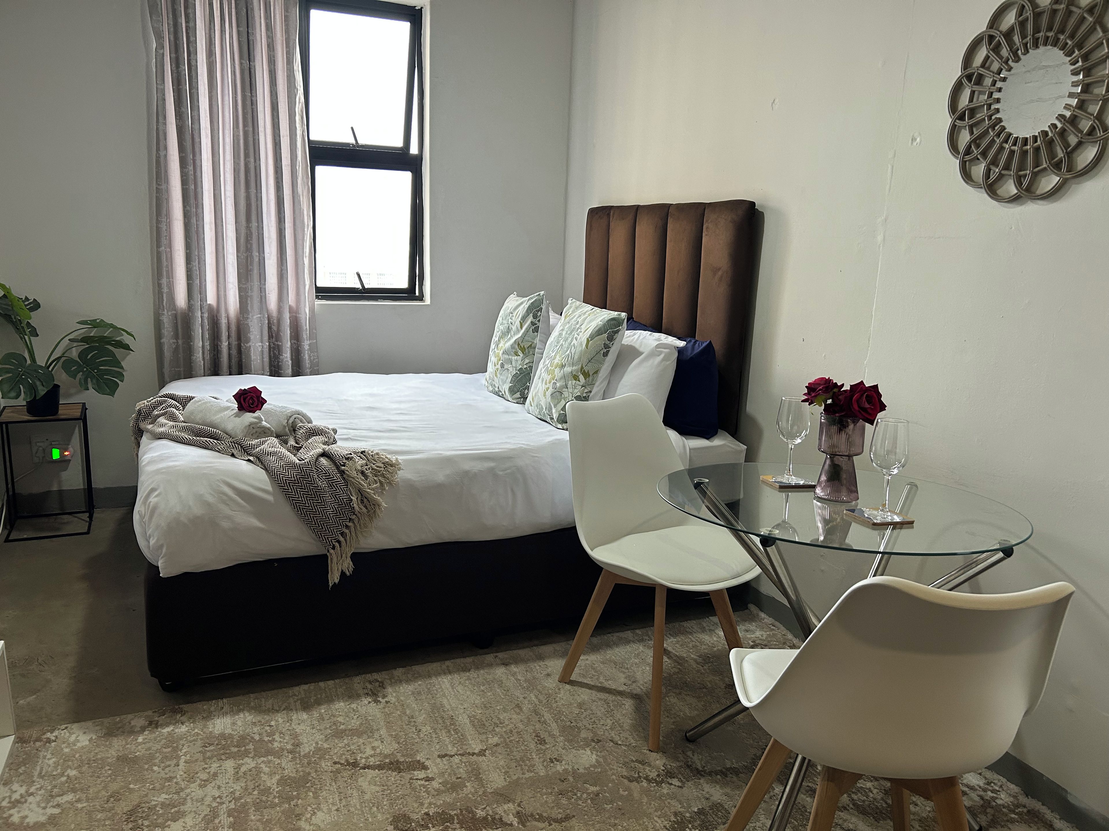 Ein Hotelzimmer mit Bett, Nachttisch, Sessel, Glastisch und einem fenster mit Vorhängen.