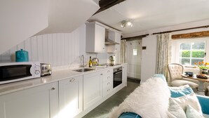 A compact kitchen with white cabinets, a microwave, a toaster, and a sink. There's a window with curtains and a chair with a table beside it. - Bank View - One Bedroom House, Sleeps 2 (Chapel Stile)