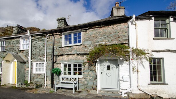 A row of stone houses with white doors and windows, a bench outside, and a clear blue sky. - Bank View - One Bedroom House, Sleeps 2 (Chapel Stile)