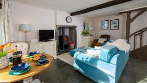 A cozy living room with a blue sofa, a fireplace, a television, and a dining area with a table set for a meal. - Bank View - One Bedroom House, Sleeps 2 (Chapel Stile)