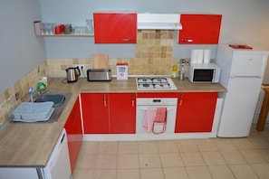 A kitchen with red cabinets, a microwave, a toaster, a sink, and a dish rack.