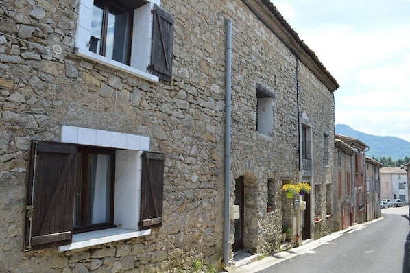A stone building with a window and a door, a narrow street, and a mountain in the background.