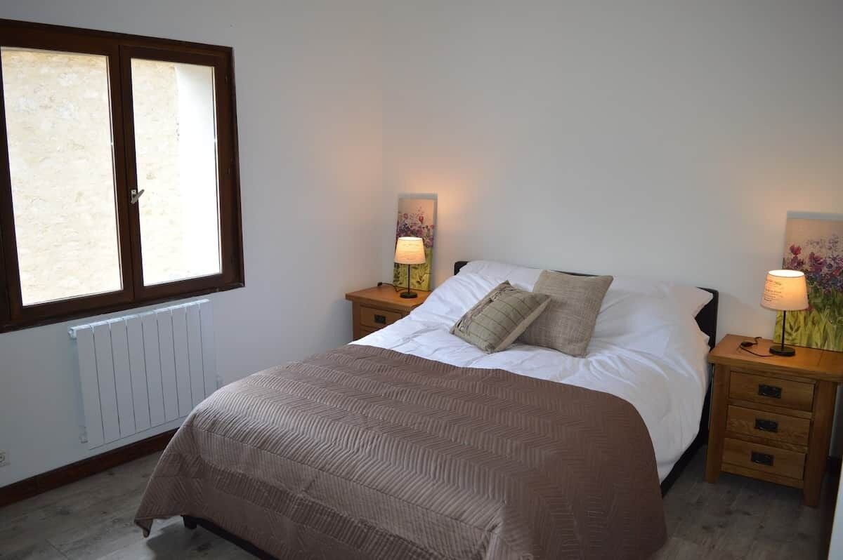 A bedroom with a bed, two bedside tables with lamps, a radiator, and a window.