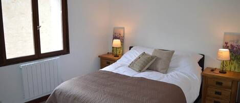 A bedroom with a bed, two bedside tables with lamps, a radiator, and a window.