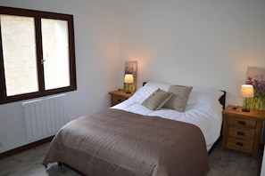 A bedroom with a bed, two bedside tables with lamps, a radiator, and a window.