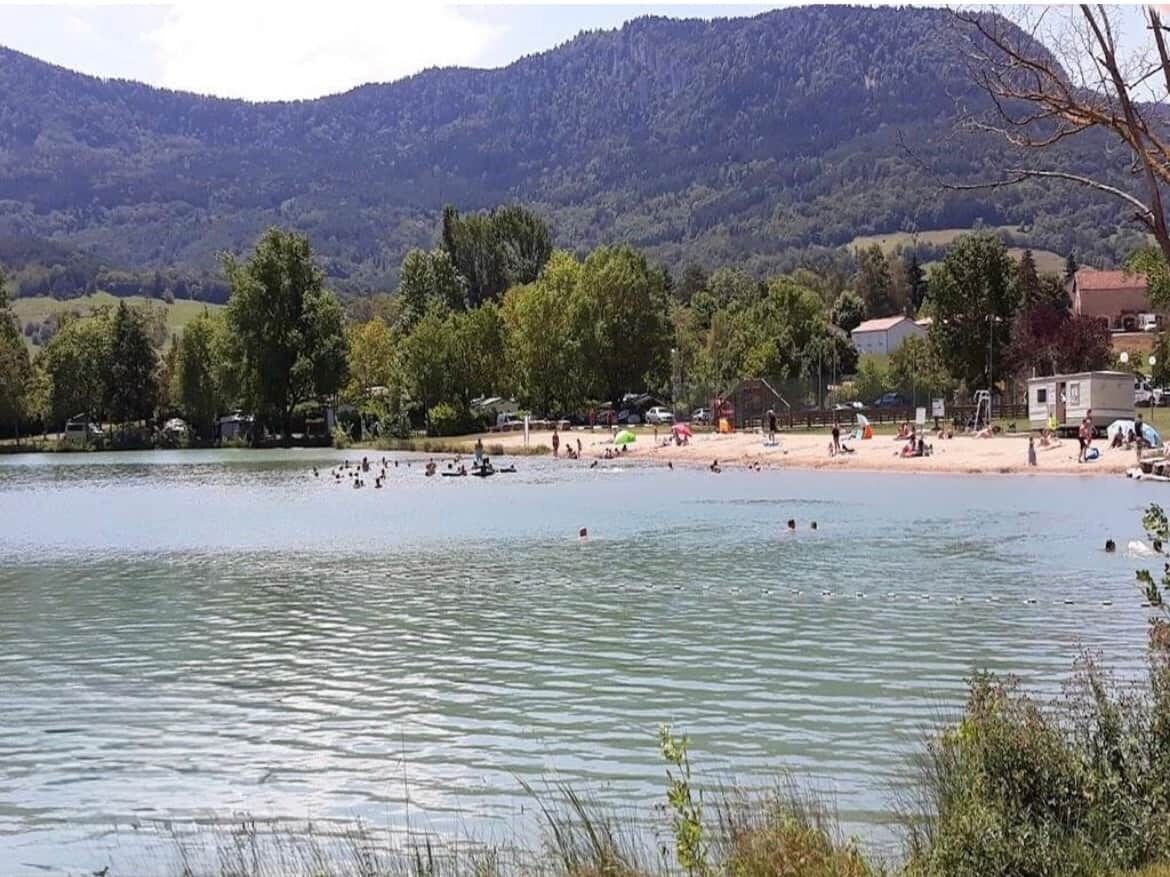 Blick auf einen See mit Strand, Bäumen und einem Berg im Hintergrund.