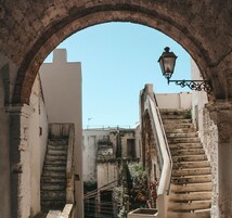 Um beco estreito com um arco de pedra, uma escadaria e um poste de luz.