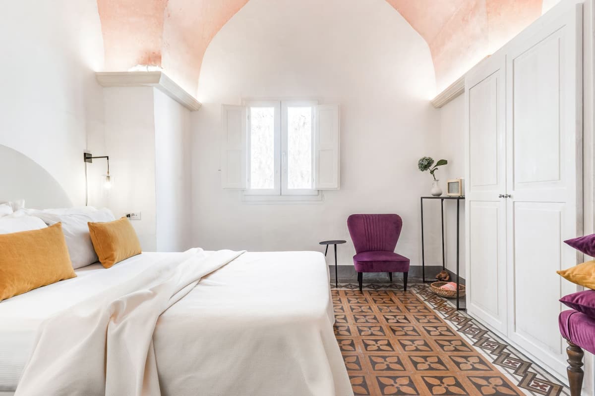 Une chambre à coucher avec un lit, une chaise, une petite table, une armoire et une fenêtre.