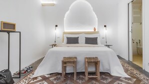 Een moderne slaapkamer met een groot bed, twee nachtkastjes, een klein tafeltje met een speaker en een kamerbreed tapijt met een patroon.