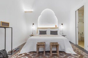 Quarto moderno com uma cama grande, duas mesas de cabeceira, uma mesinha com um alto-falante e um tapete estampado.