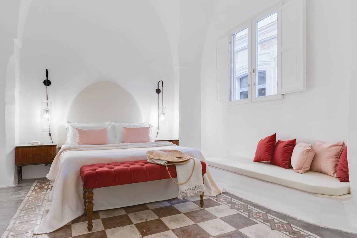 Une chambre à coucher avec un lit, des tables de chevet, un banc et un sol à motifs.