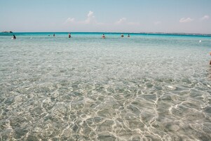 Uma praia com águas cristalinas e pouco profundas, e barcos ao longe.