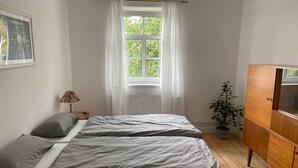 Un dormitorio con dos camas, un radiador, una ventana con cortinas, una lámpara y un armario de madera.