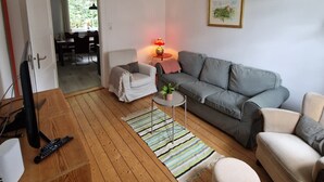 Una sala de estar con un sofá gris, un sillón blanco, una mesa de centro de madera, un tapete a rayas y una araña.