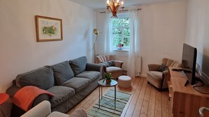 Una sala de estar con un sofá gris, un sillón beige, una mesa de centro de madera y un televisor sobre un mueble de madera.