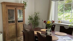 Un comedor con una mesa de madera, sillas de metal, un armario y una ventana con vista a follaje.