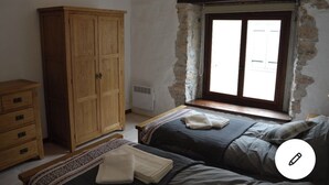 A bedroom with a large wooden wardrobe, a bed with a grey blanket, and a window with a curtain. - Lovely renovated Cottage in Puivert (Puivert)