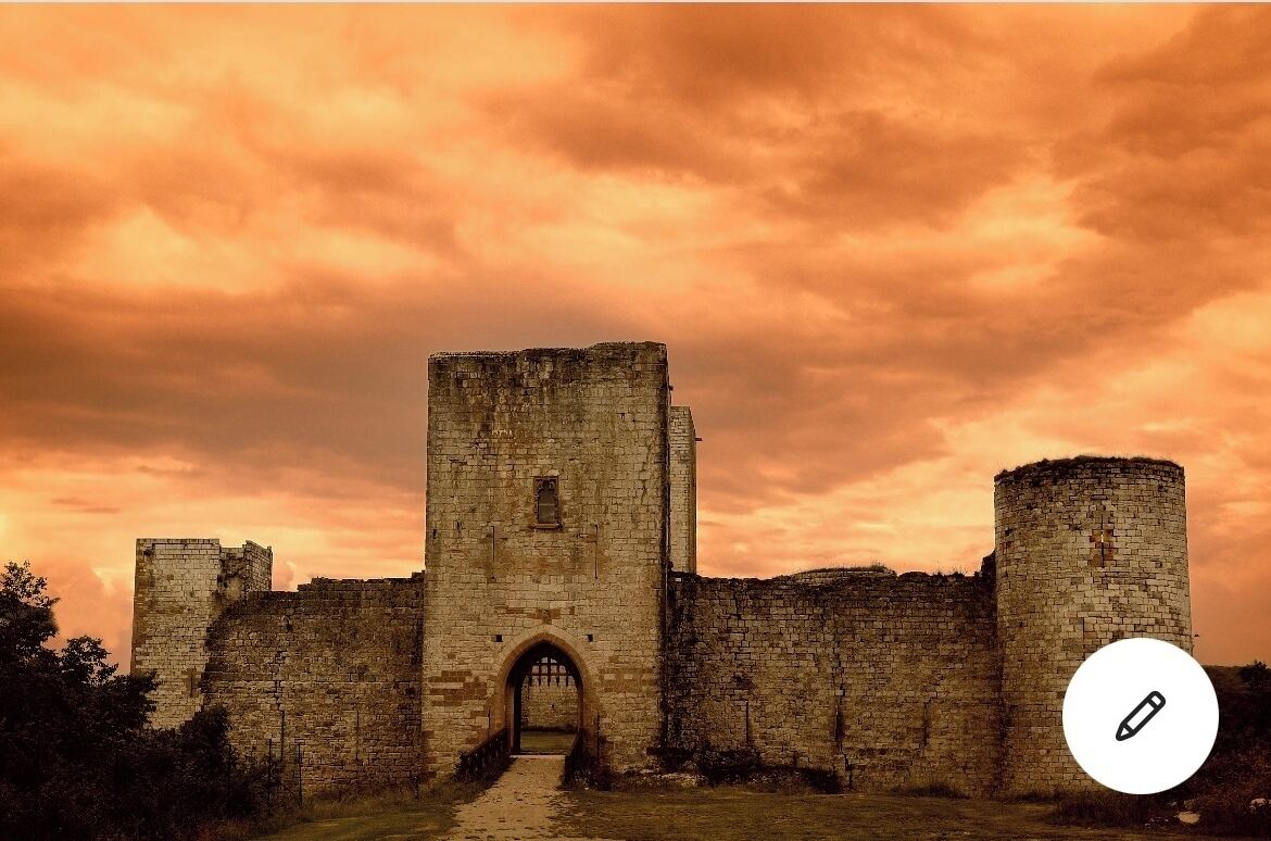 Eine historische Burg aus Stein mit einem zentralen Rundbogenportal, umgeben von Mauern und Türmen, unter einem beeindruckenden Abendhimmel.