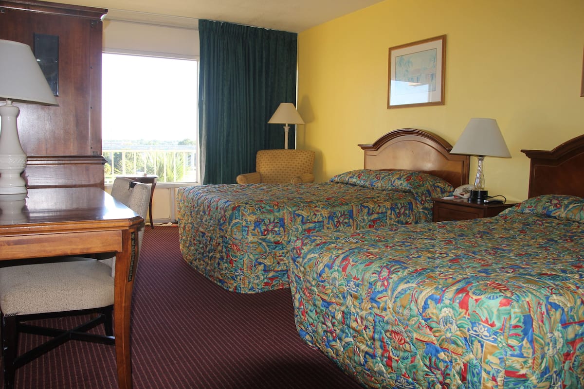 A hotel room with two beds, a desk, a chair, and a window with curtains.