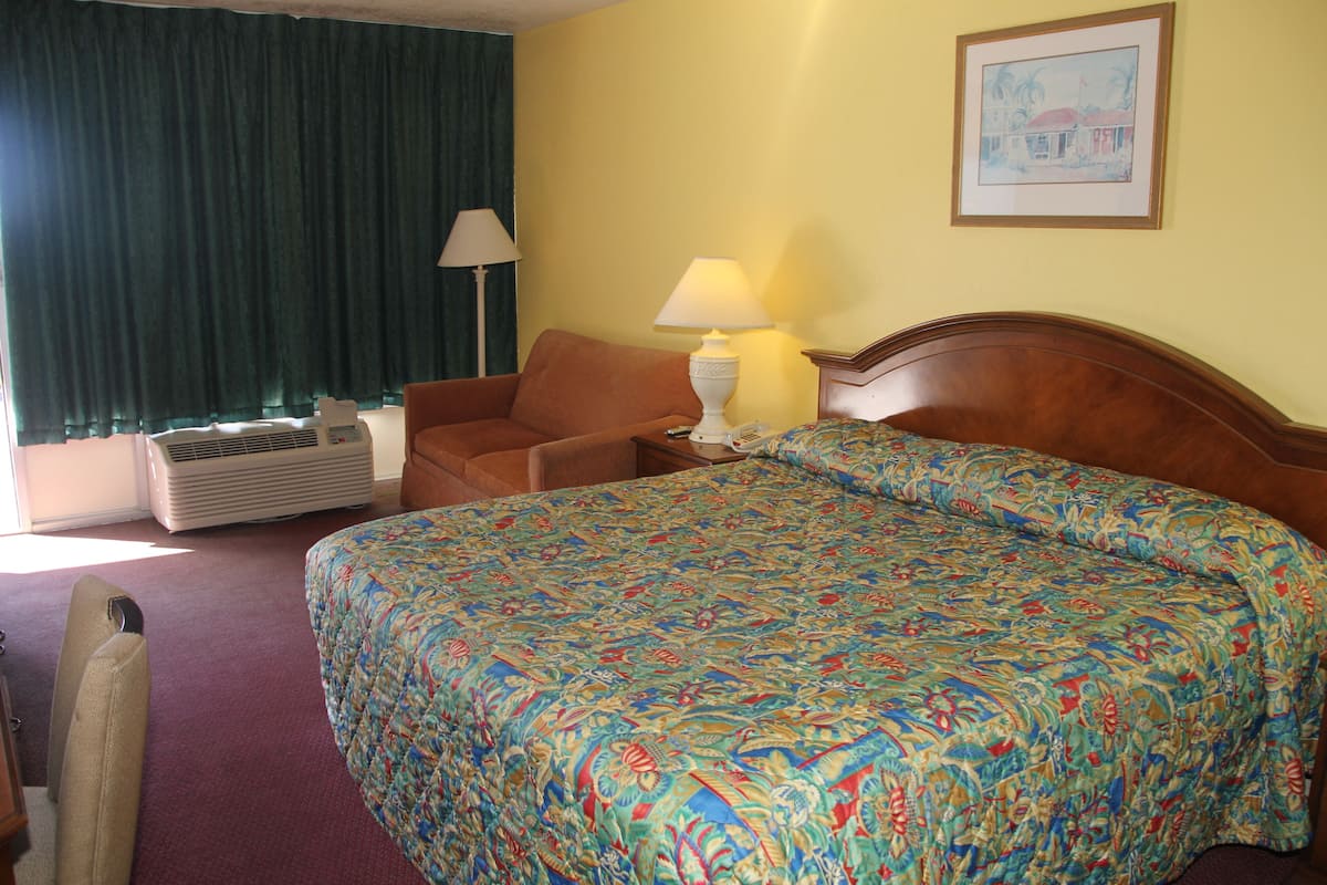 A hotel room with a large bed, a chair, a lamp, and a painting on the wall.