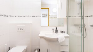 Une salle de bain moderne avec une douche à parois de verre, un lavabo blanc avec un miroir au-dessus et des toilettes.