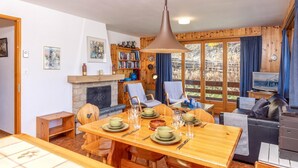 Un intérieur de chalet chaleureux comprenant un coin repas, une cheminée, un téléviseur et une bibliothèque.