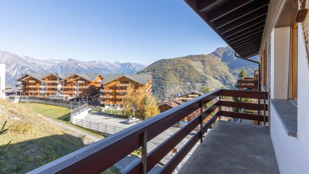 Un chalet de montagne doté de plusieurs balcons en bois et offrant une vue sur des montagnes enneigées.