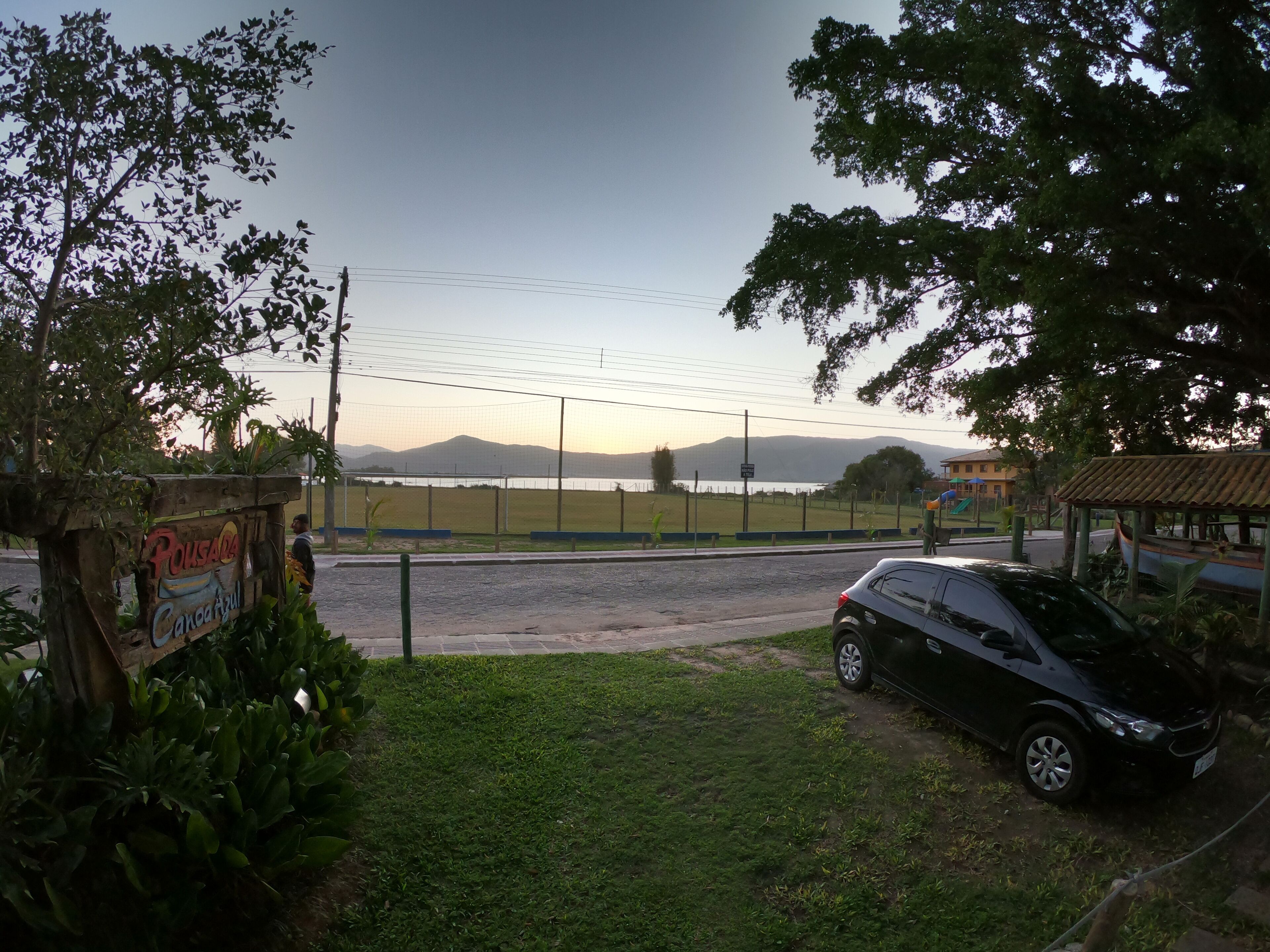 A paved road with a black car parked on the side, a grassy area, and a signboard with text.