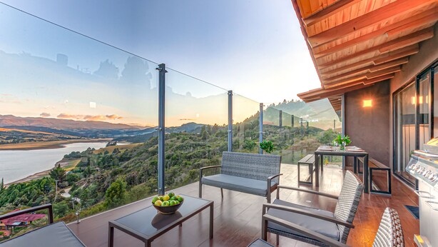 Un balcon avec vue sur une rivière et des collines, aménagé avec une table, des chaises et un panier de fruits.