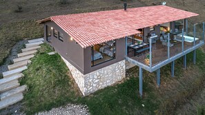 Een modern huis met een rode pannendak, een stenen fundering en een glazen balkon.
