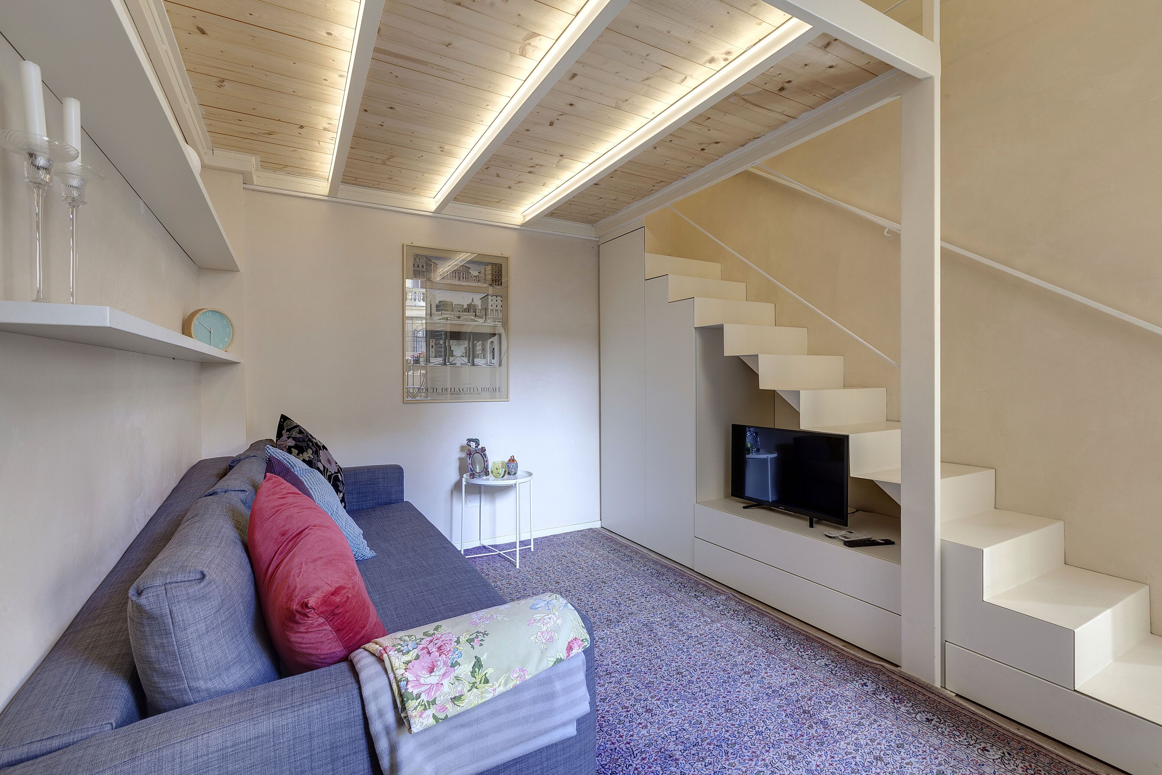 A modern living room with a sofa, a small table, a TV, and a staircase.